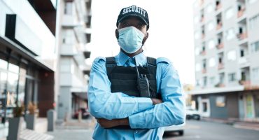Portrait of a confident masked young security guard standing guard outdoors