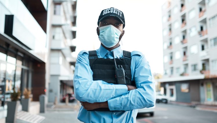 Portrait of a confident masked young security guard standing guard outdoors