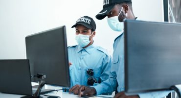 Shot of two masked young security guards on duty at the front desk of an office